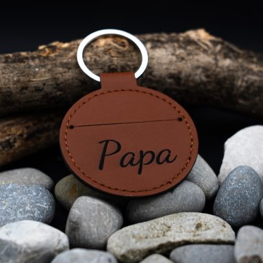 Brauner Schlüsselanhänger mit der Aufschrift "Papa" auf grauen Steinen.