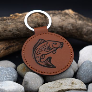 Brauner Schlüsseletikett mit geprägtem Fisch-Motiv, auf Steinen und Holz präsentiert.