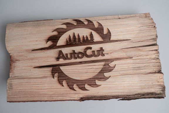 Holzplatte mit eingraviertem Logo von AutoCut und einem Sägeblatt-Motiv.