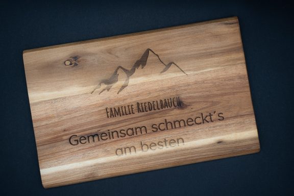 Holzplatte mit eingravierter Landschaft und Text "Gemeinsam schmeckt's".