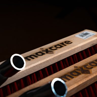 Holzregal mit roten Bürsten und "maxcare"-Logo auf einem schwarzen Hintergrund.
